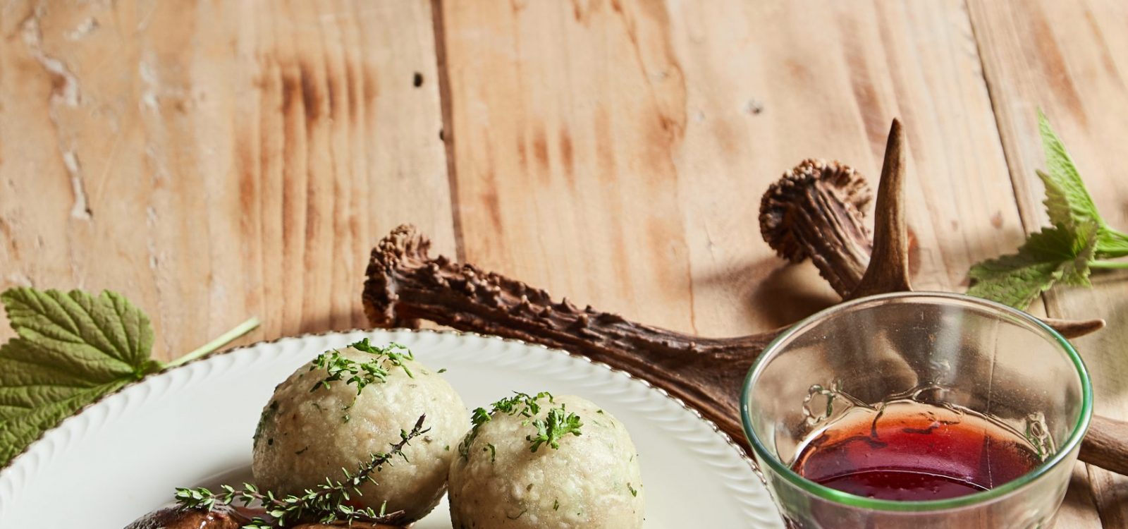 Gourmet wild venison goulash with dumplings and shredded red cabbage served with a glass of red wine on a table with decoration of antlers and copy space